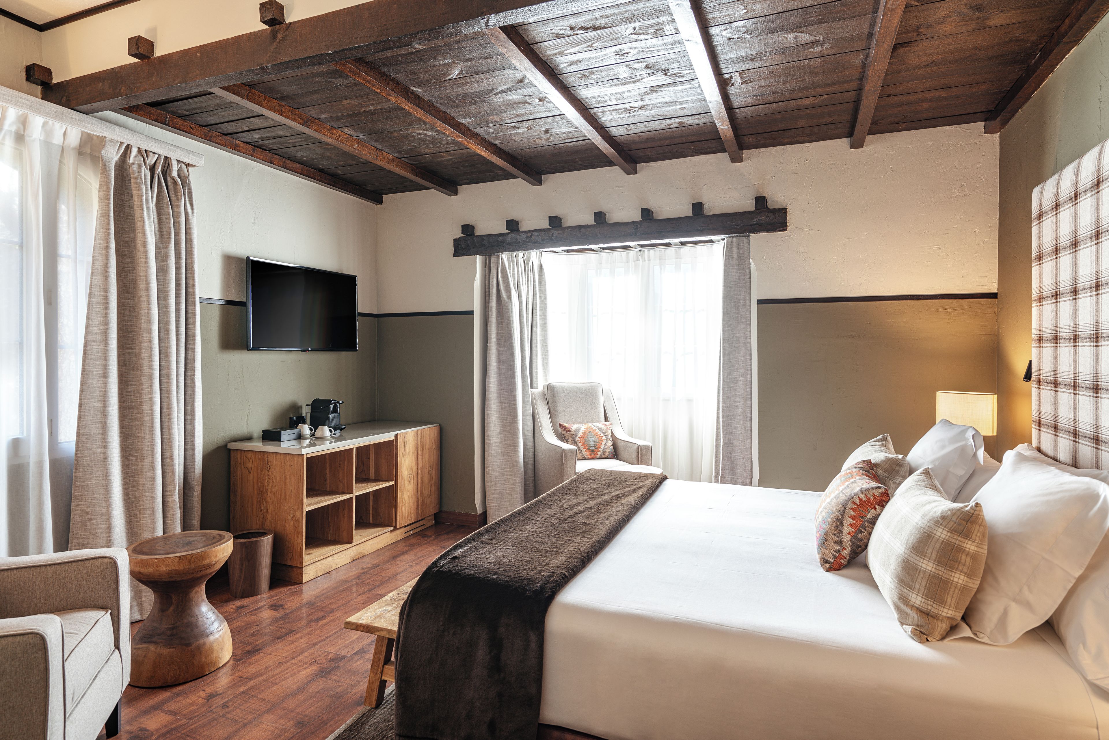 A hotel room with a bed, a desk, a chair, a TV, and a window with curtains.