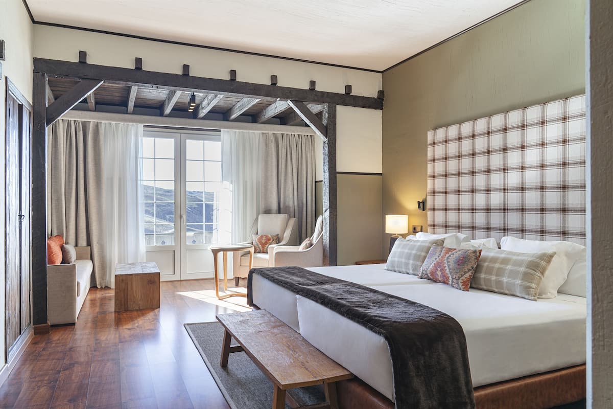 Habitación de hotel con una cama grande, un banco, una silla y una mesita.