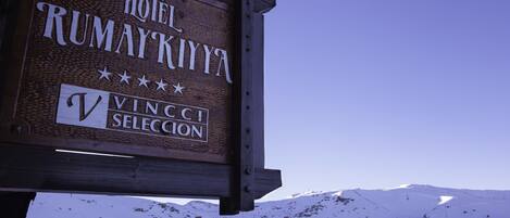 Un letrero de madera del Hotel Rumaykiya con montañas al fondo.