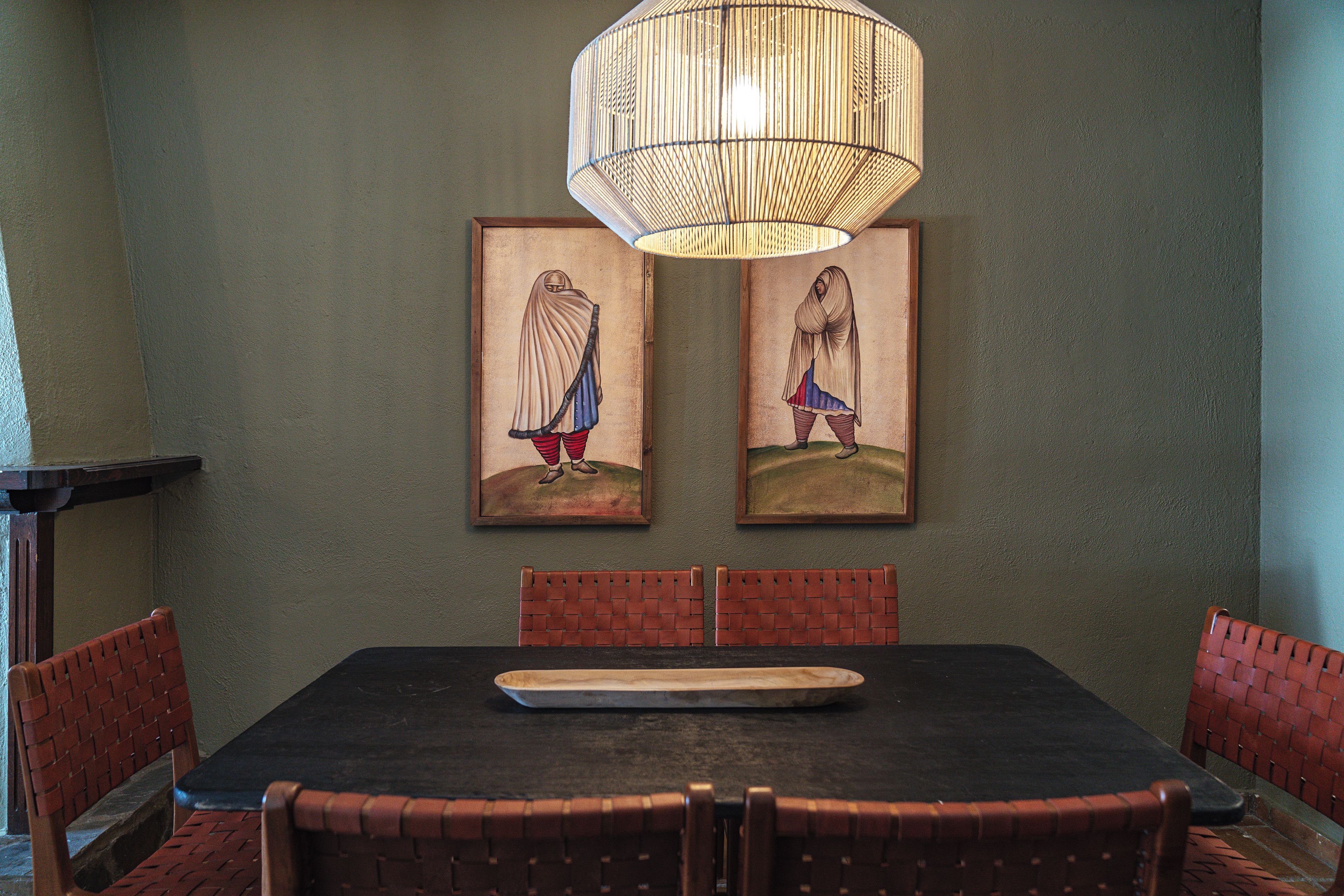 A dining area with a black table, red woven chairs, and two framed artworks on the wall.