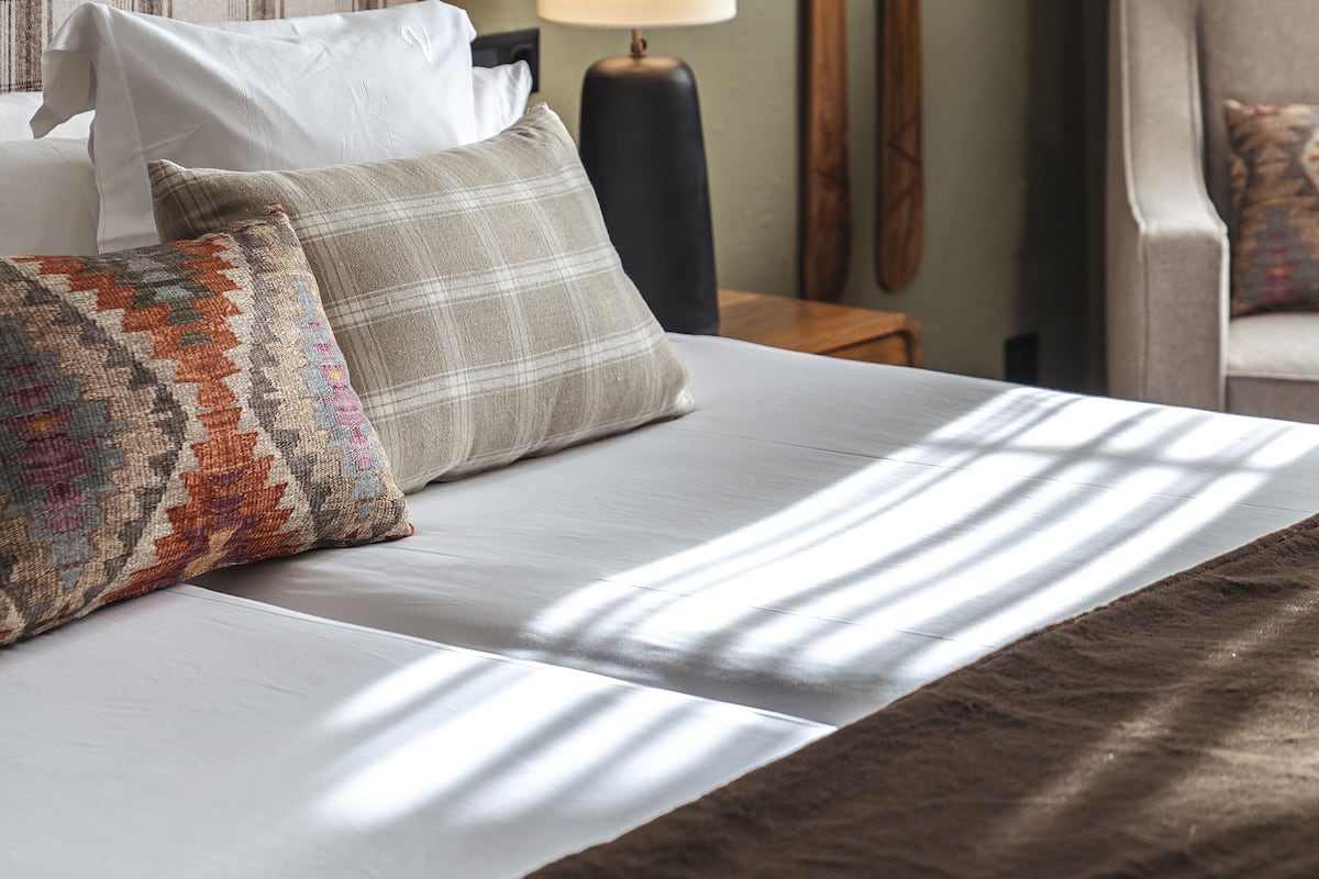 Habitación de hotel con cama, almohadas, lámpara y esquíes apoyados en la pared.