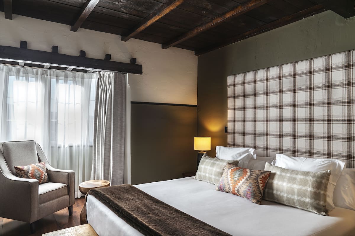 Habitación de hotel con una cama grande, una silla, una mesita de noche y un cabecero estampado con un diseño escocés.