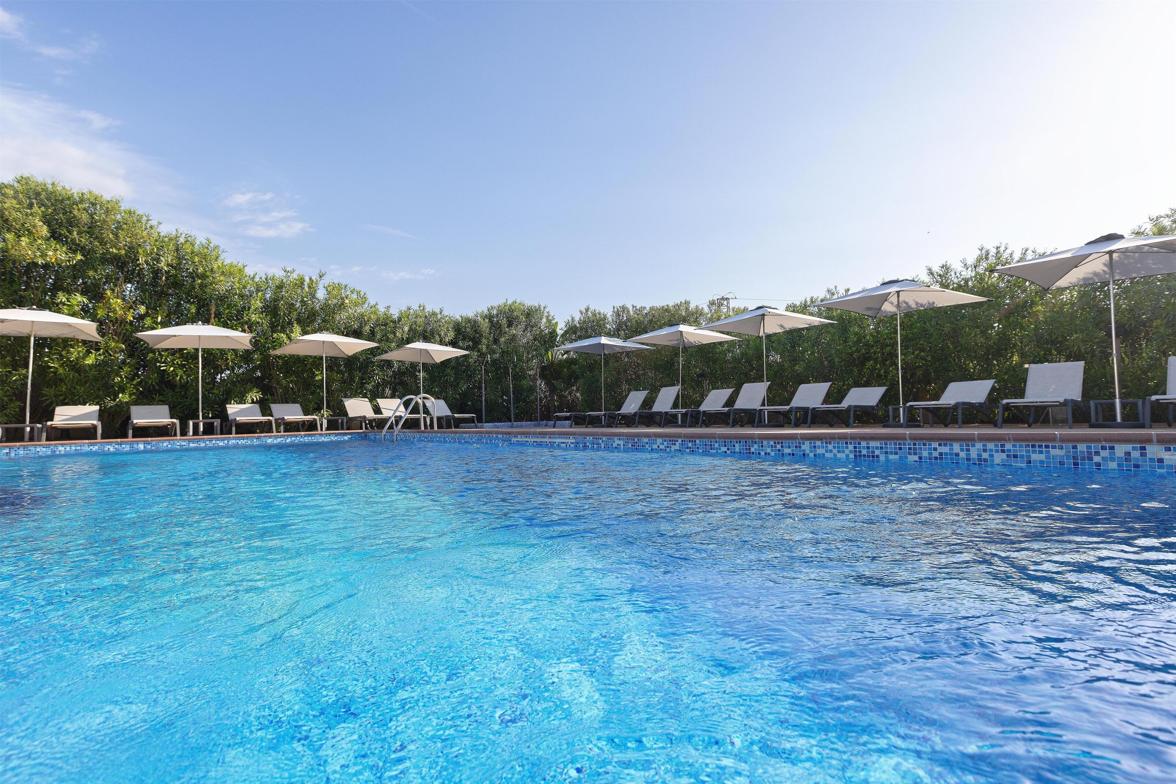 A swimming pool with lounge chairs and umbrellas, surrounded by trees.