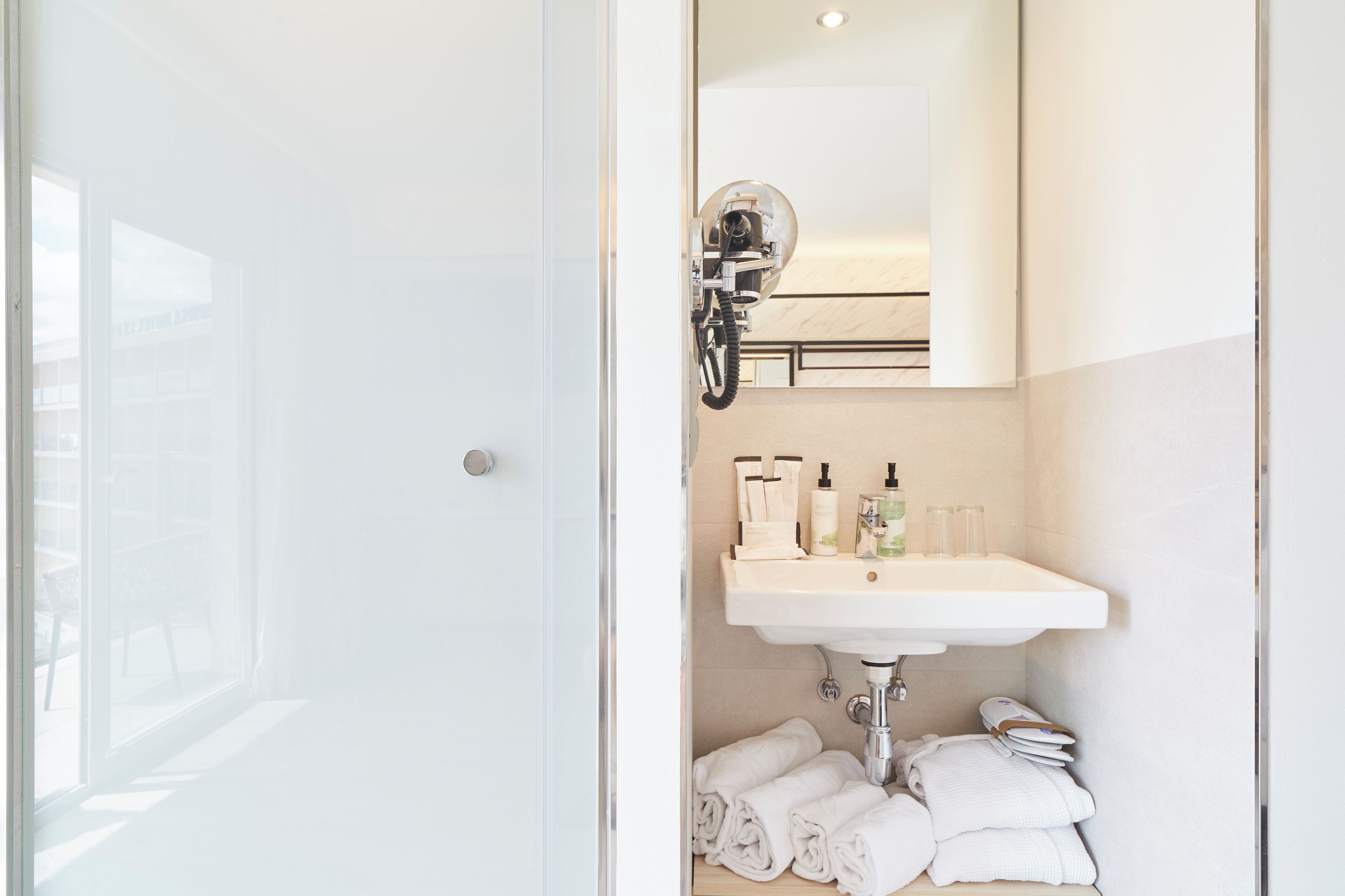 A bathroom with a glass shower door, a white sink with toiletries, and neatly folded towels.
