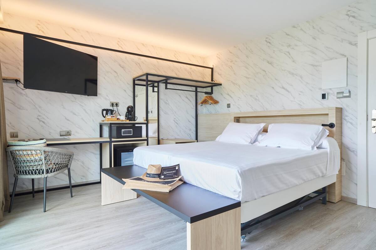 Une chambre d’hôtel moderne équipée d’un lit, d’un bureau, d’une chaise et d’un téléviseur fixé au mur.