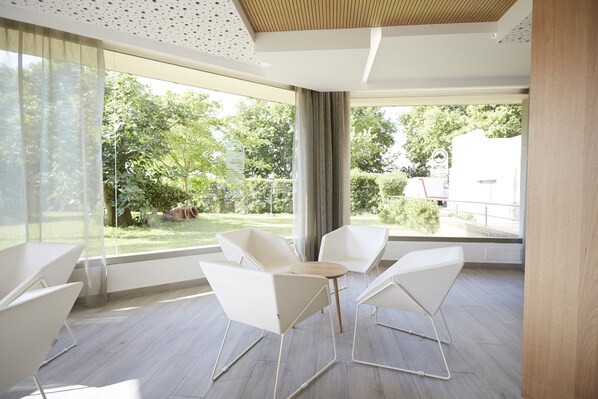 Quarto moderno com grandes janelas, mobiliário branco e vista para o verde lá fora.