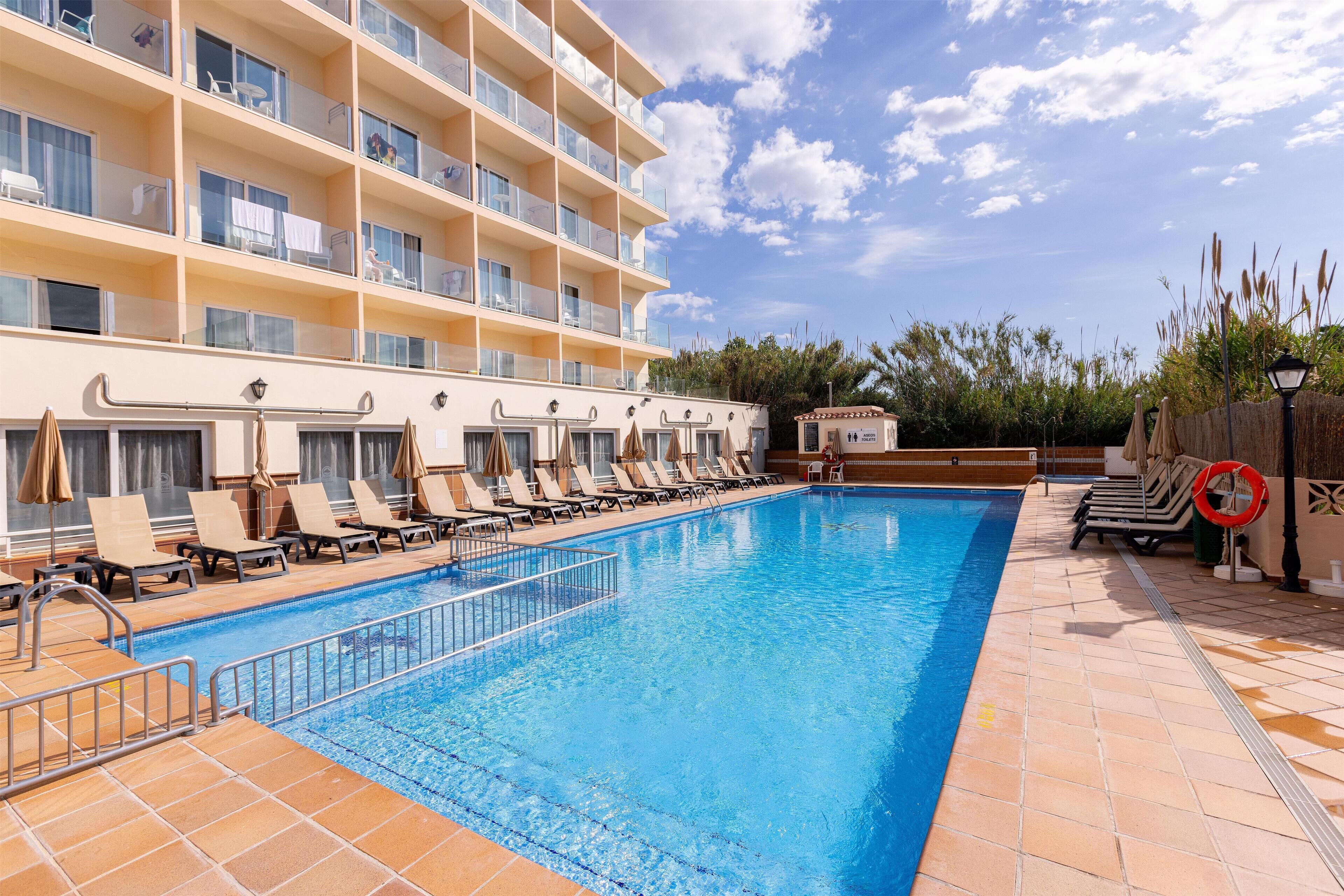 A swimming pool with lounge chairs and a building with multiple balconies.
