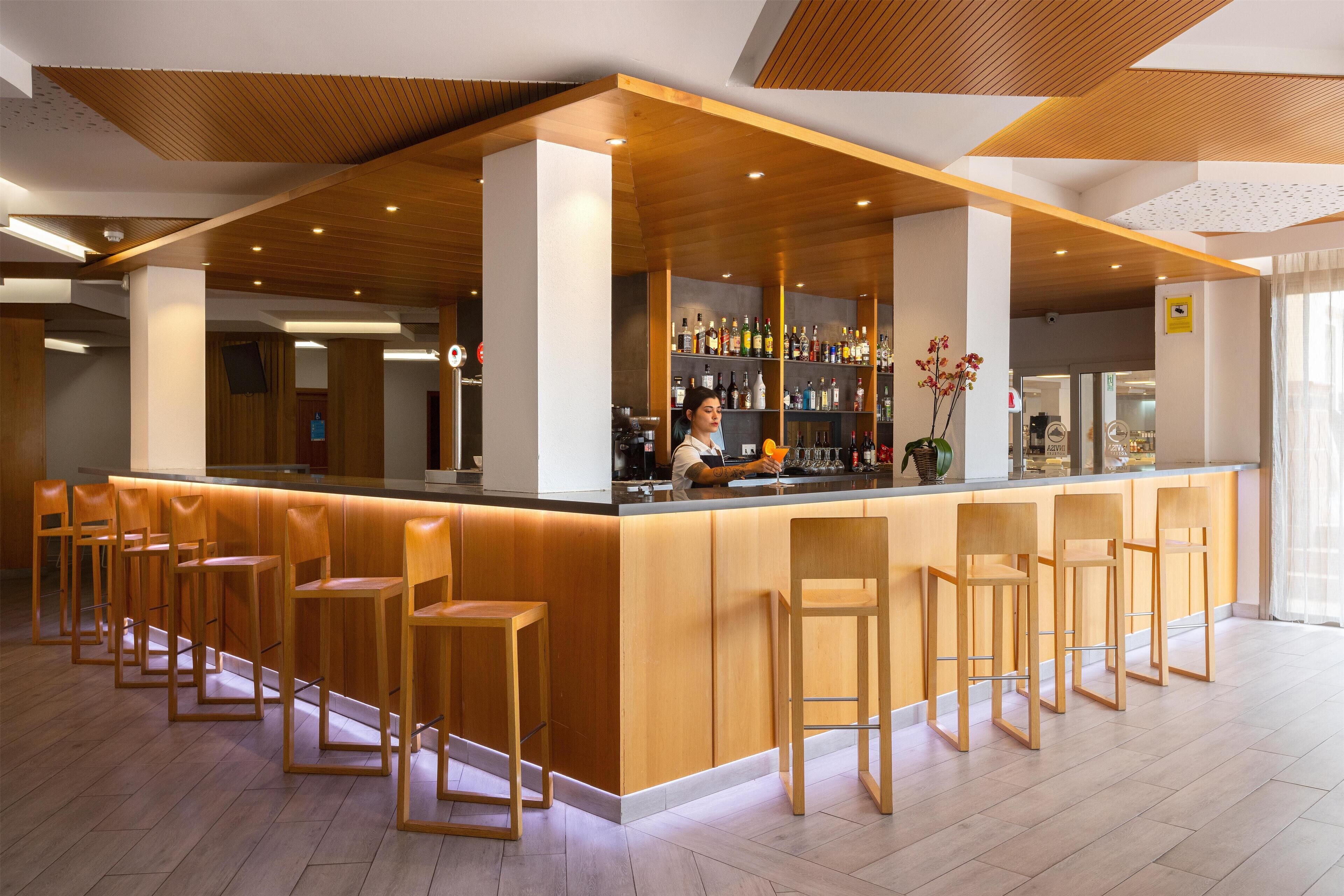 Un espace bar moderne avec des tabourets de bar en bois et un barman.