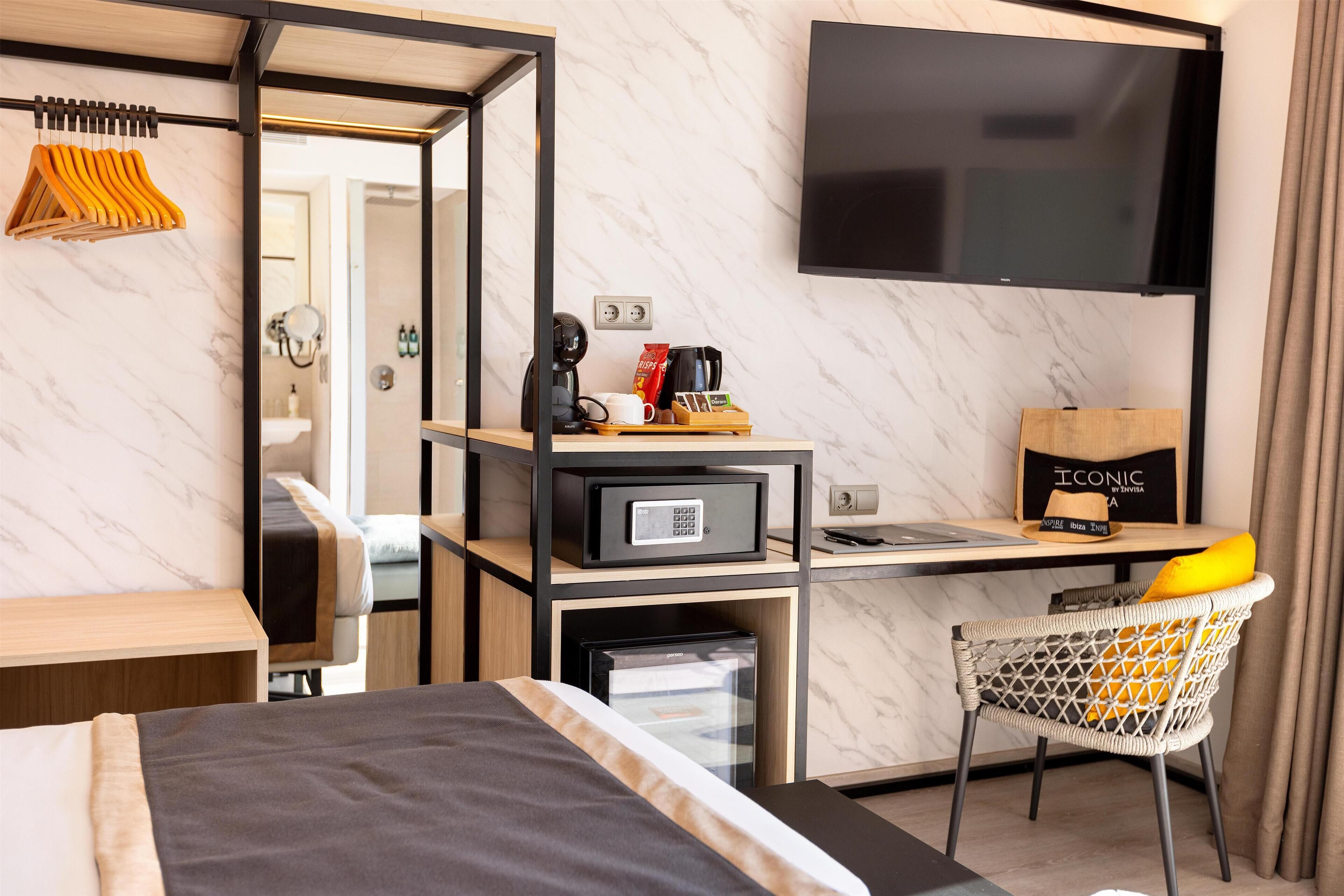 Habitación de hotel con cama, escritorio, computadora, televisión, mini bar y una silla.