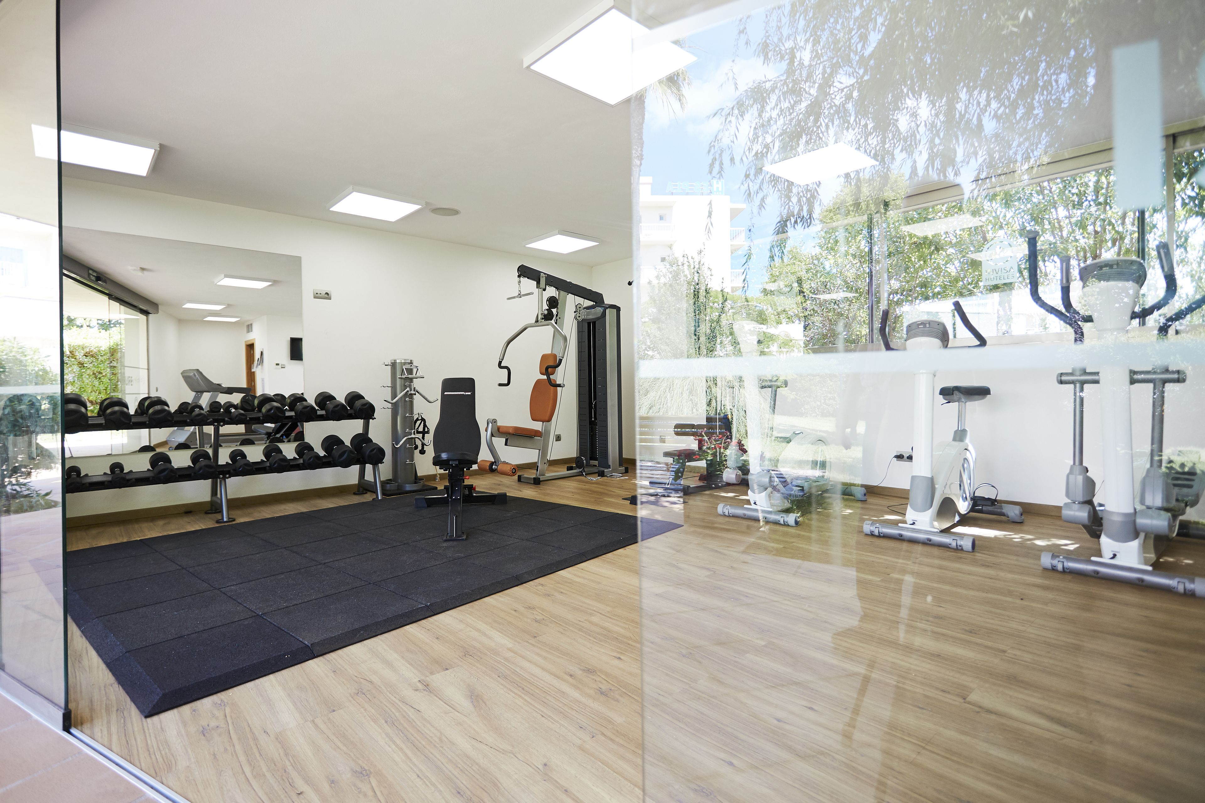 Un gimnasio con equipo de ejercicio, un espejo y vistas al exterior.