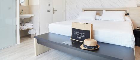 A hotel room with a bed, a nightstand, a bedside table, a mirror, a towel rack, and a sign on the wall.
