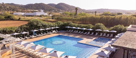 A pool area with multiple sun loungers and umbrellas, surrounded by a landscaped garden and a view of distant hills.