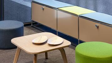 A small, modern room with a wooden table, two stools, and a green ottoman.