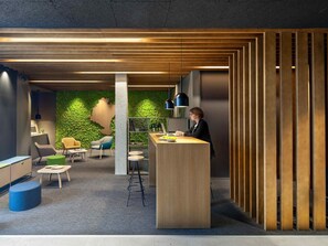 A modern office space with a wooden reception desk, a green wall, and a seating area with chairs and tables. - ibis Styles Pamplona Noain (Noain)