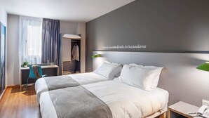 Una habitación de hotel moderna con una cama grande, un escritorio, una silla y un armario.