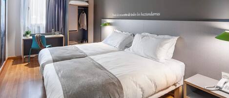 A modern hotel room with a large bed, a desk, a chair, and a wardrobe.