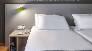 Ein Hotelzimmer mit einem ordentlich bezogenen Bett, einem Nachttisch mit Lampe, einem Glas Wasser und einer Zeitschrift.