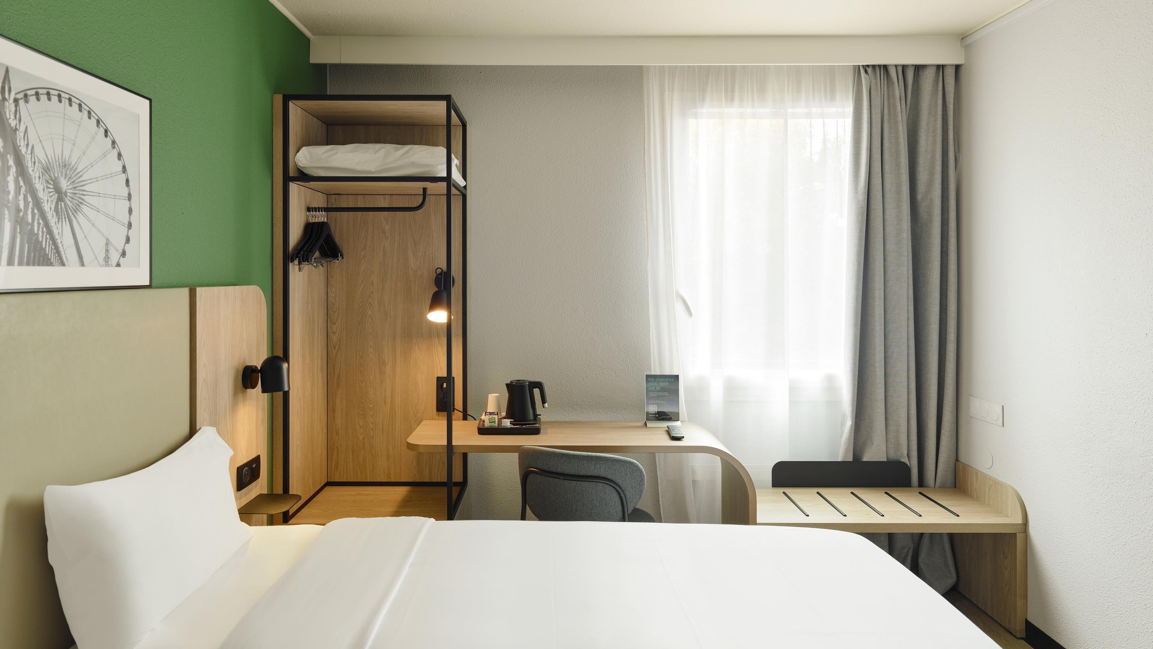 A hotel room with a bed, a desk with a chair, a shower, and a window with curtains.