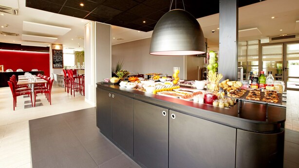 Uma área de refeições moderna com balcão de buffet, cadeiras vermelhas e uma luminária pendente grande.
