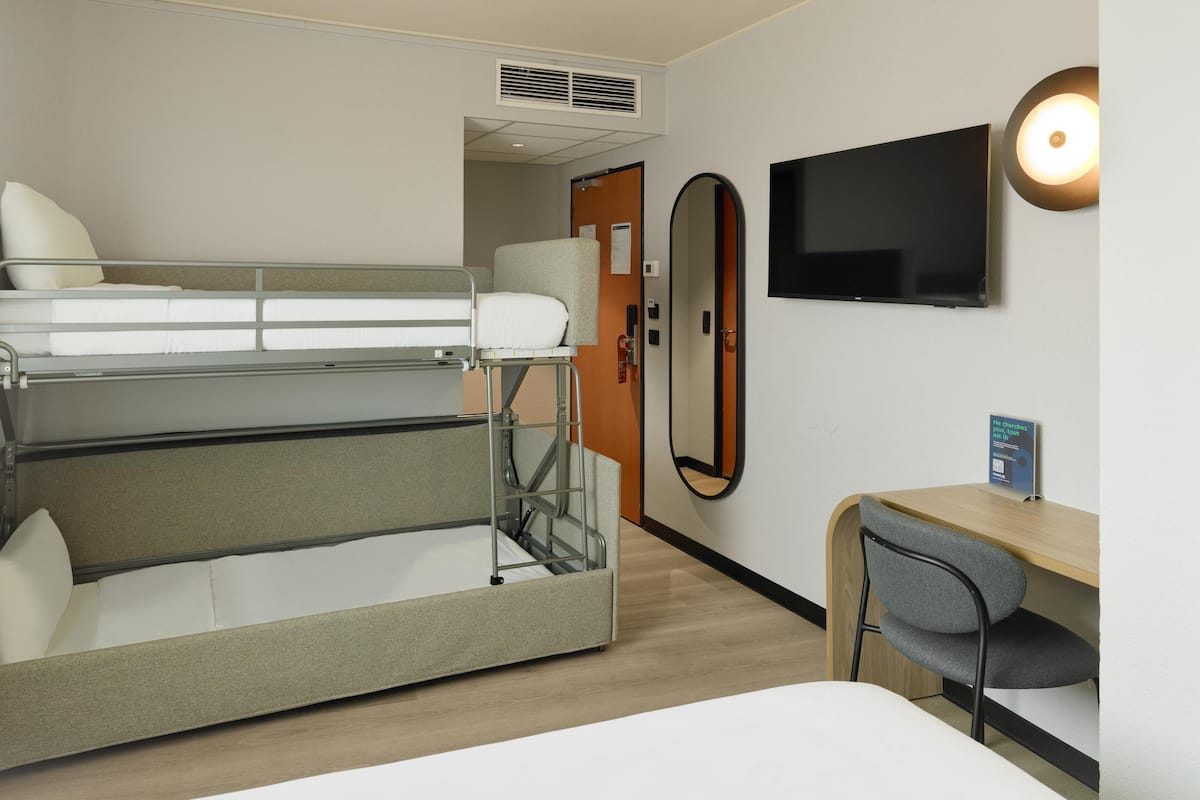 Ein Hotelzimmer mit Etagenbett, Schreibtisch mit Stuhl, Flachbildfernseher und Spiegel.