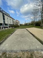 Un patio con área de concreto, un edificio con la leyenda "Campaill Hotel Restaurant", mesas al aire libre y abundante follaje.