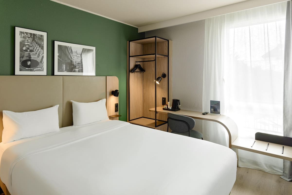 Ein Hotelzimmer mit einem großen Bett, einem Schreibtisch mit Stuhl, einem Spiegel und zwei gerahmten Bildern an der Wand.
