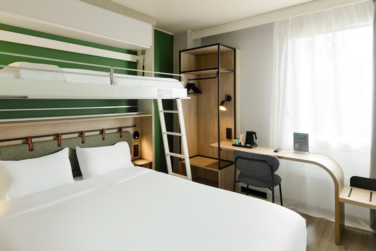 Camera d'albergo con un letto a castello, una scrivania con una sedia, una scala e un tavolino con una macchina per il caffè.