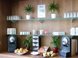 Una estación de café con varias máquinas de espresso, diferentes tipos de tazas de café y una selección de frutas y aperitivos.