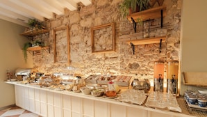 Una mesa de buffet con diversos alimentos y bebidas, un fondo de pared de piedra y un suelo con estampado de cuadros.