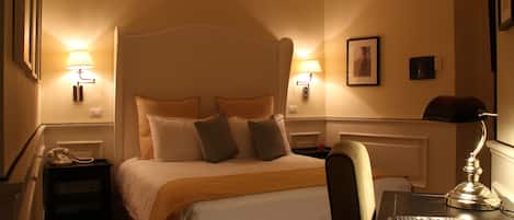 Ett hotellrum med en stor säng, sänglampor, ett skrivbord med en lampa och en stol.