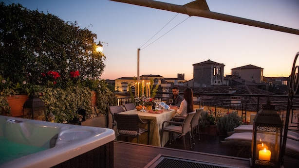 Una terraza en la azotea con un jacuzzi, una mesa de comedor, sillas y un farol iluminado con velas.