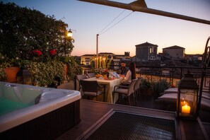 Una terraza en la azotea con un jacuzzi, una mesa de comedor, sillas y un farol iluminado con velas.