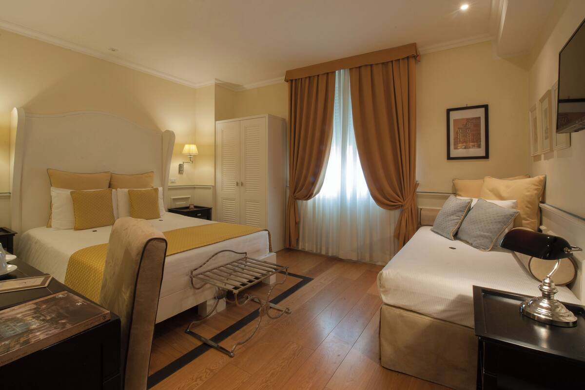 A hotel room with two beds, a desk, a chair, a lamp, and a window with curtains.