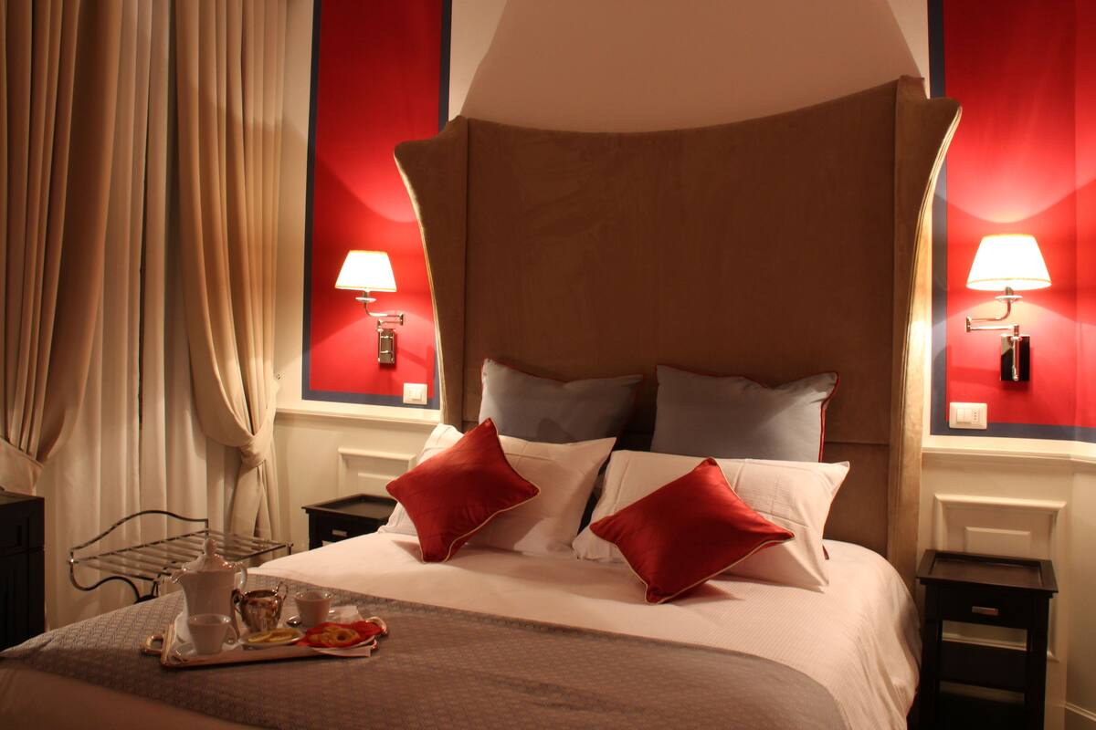 A hotel room with a large bed, red accent walls, two bedside lamps, and a tray with breakfast items.
