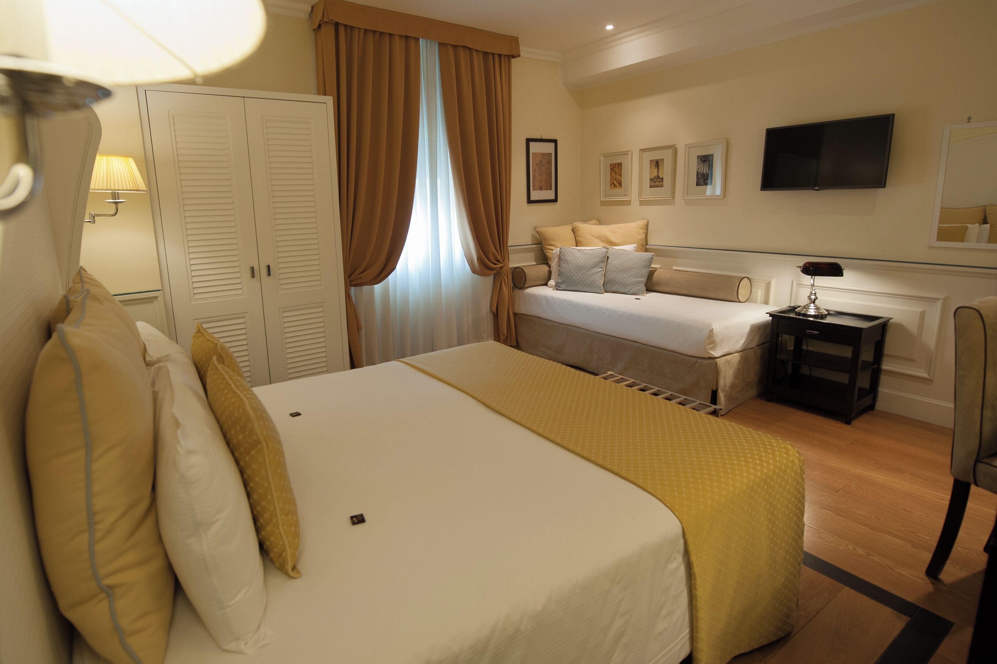 A hotel room with a large bed, a smaller bed, a TV, a desk, and a wardrobe.