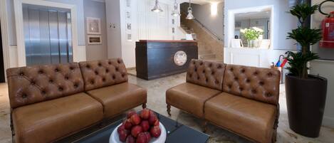 A spacious living room with a brown leather sofa set, a black coffee table with a bowl of fruit, and a modern kitchen in the background.