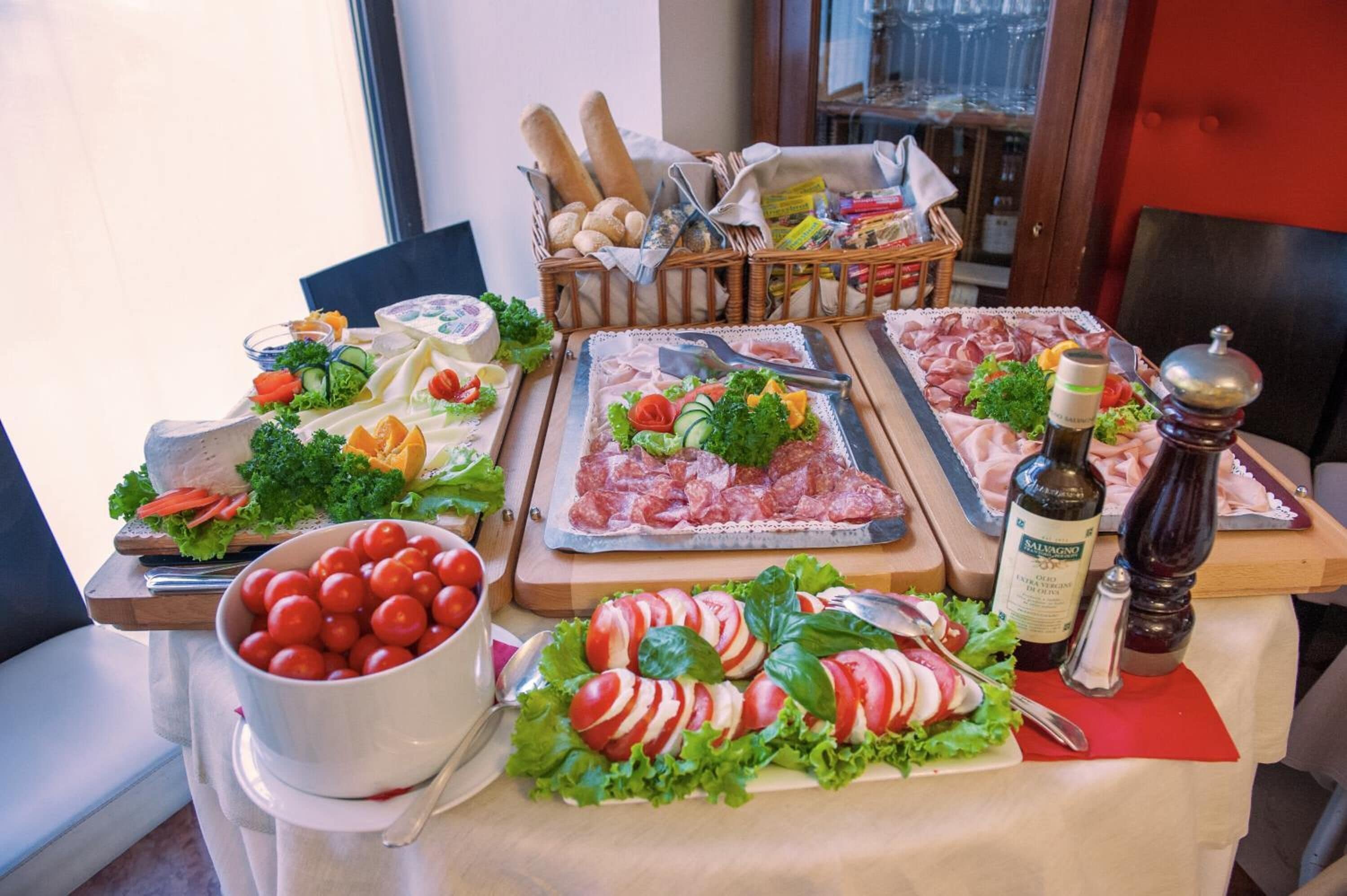 A table with various food items including tomatoes, cheese, and meats, with a basket of bread and condiments in the background.