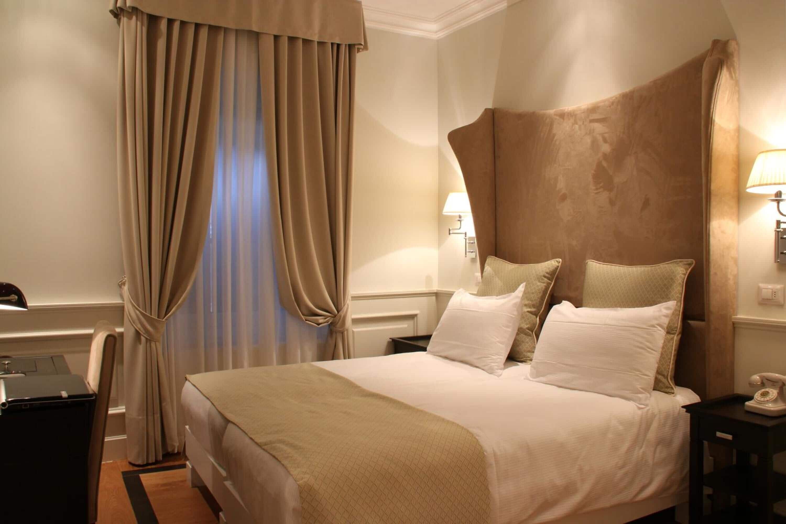 A hotel room with a large bed, beige curtains, a desk, and a lamp.
