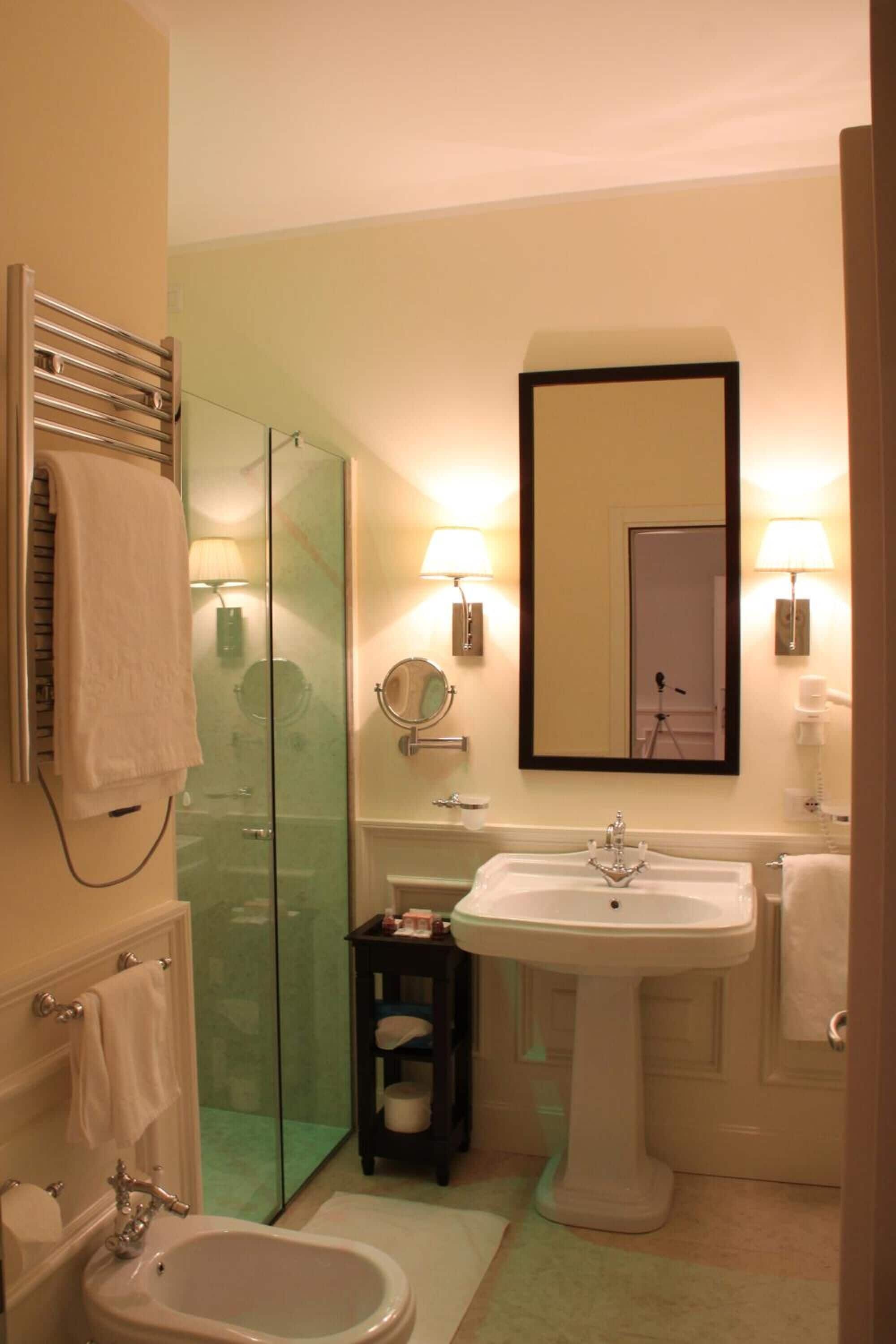 Une salle de bain avec une douche en verre, un lavabo sur colonne, un grand miroir et des toilettes.