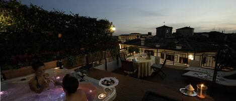 Terraza en la azotea con jacuzzi, zona de comedor y vistas a la ciudad al atardecer.