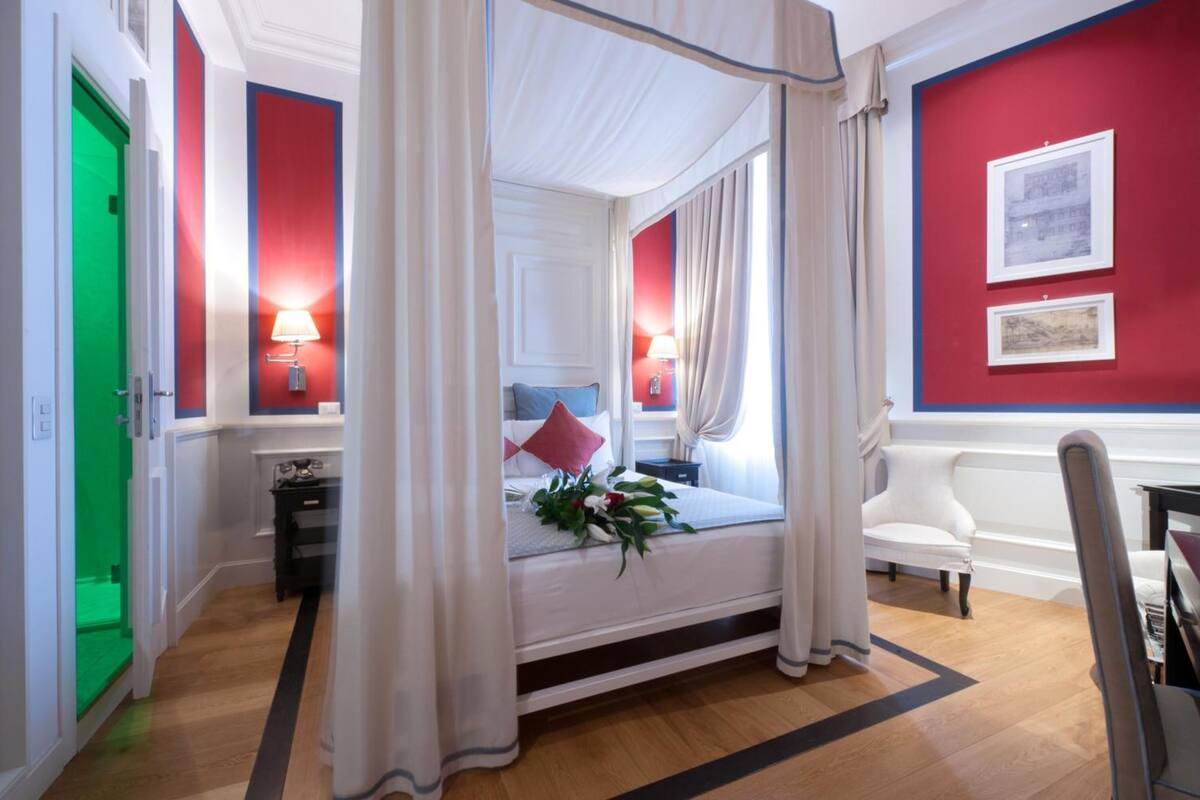 A hotel room with a four-poster bed, a green door, red walls, and two bedside lamps.