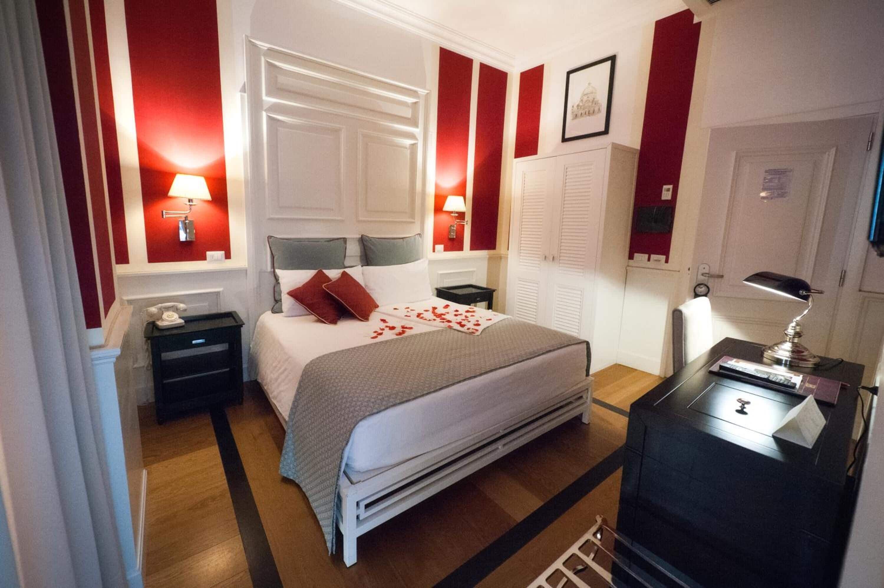 Ett hotellrum med en säng, sängbord, ett skrivbord med en lampa och en garderob.