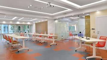 Una sala de conferencias moderna con mesas y sillas blancas, un proyector y un separador de vidrio.
