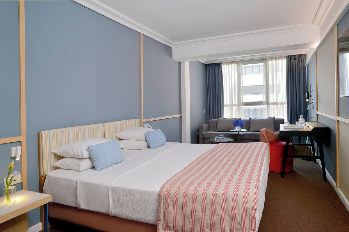 A hotel room with a large bed, a desk, a chair, and a sofa.