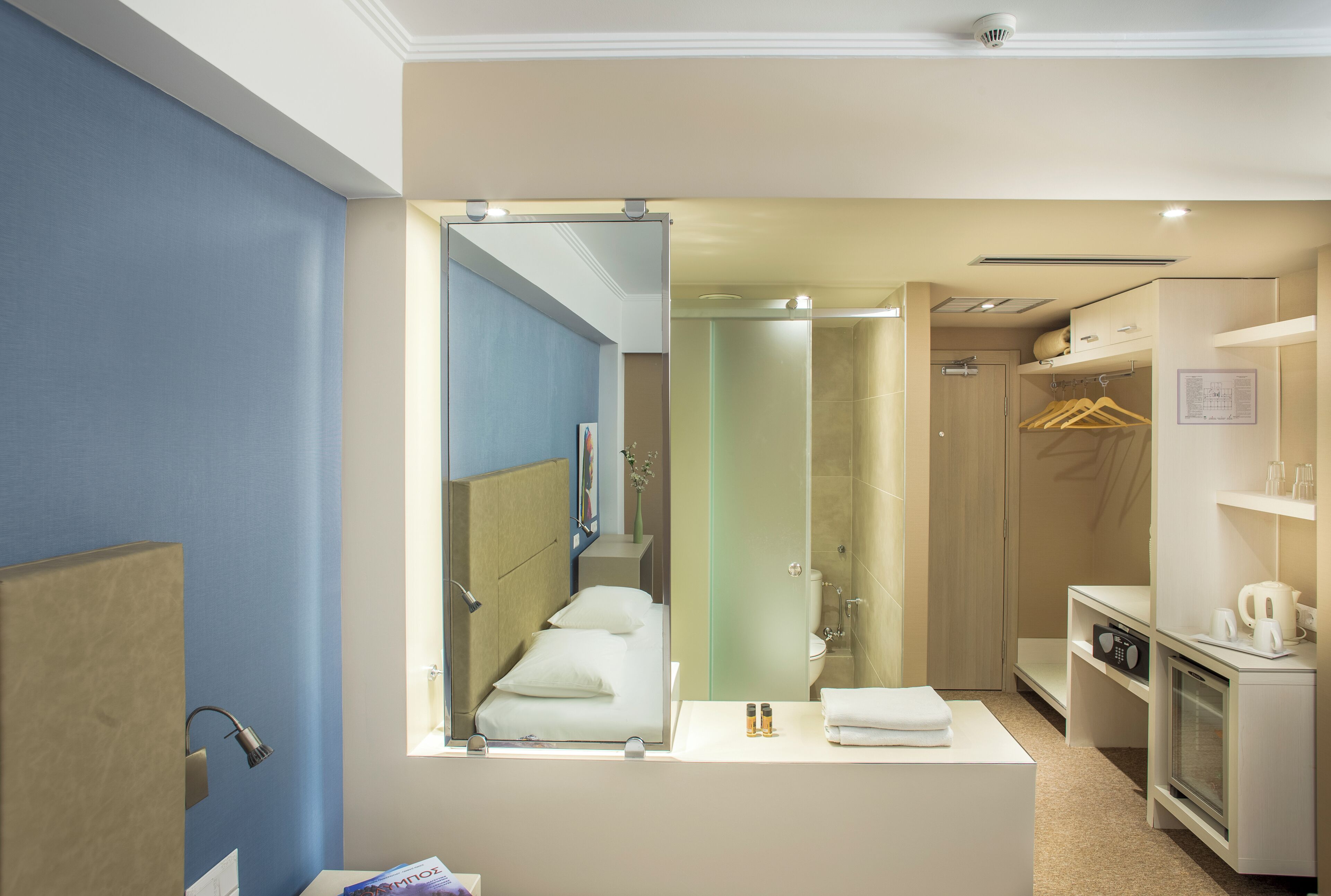 Et moderne badeværelse med et stort spejl, en brusekabine, et håndvaskområde med toiletartikler og et walk-in closet.
