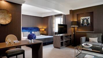 A modern hotel room with a bed, a TV, a sofa, a coffee table, and a desk with a lamp and vase.
