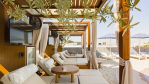A sunlit outdoor seating area with a wooden pergola, cushioned sofas, and a round table. - Airotel Alexandros Hotel (Athens)