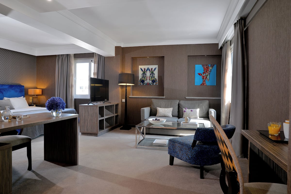 A modern hotel room with a bed, a sofa, a coffee table, a TV, and artwork on the walls.
