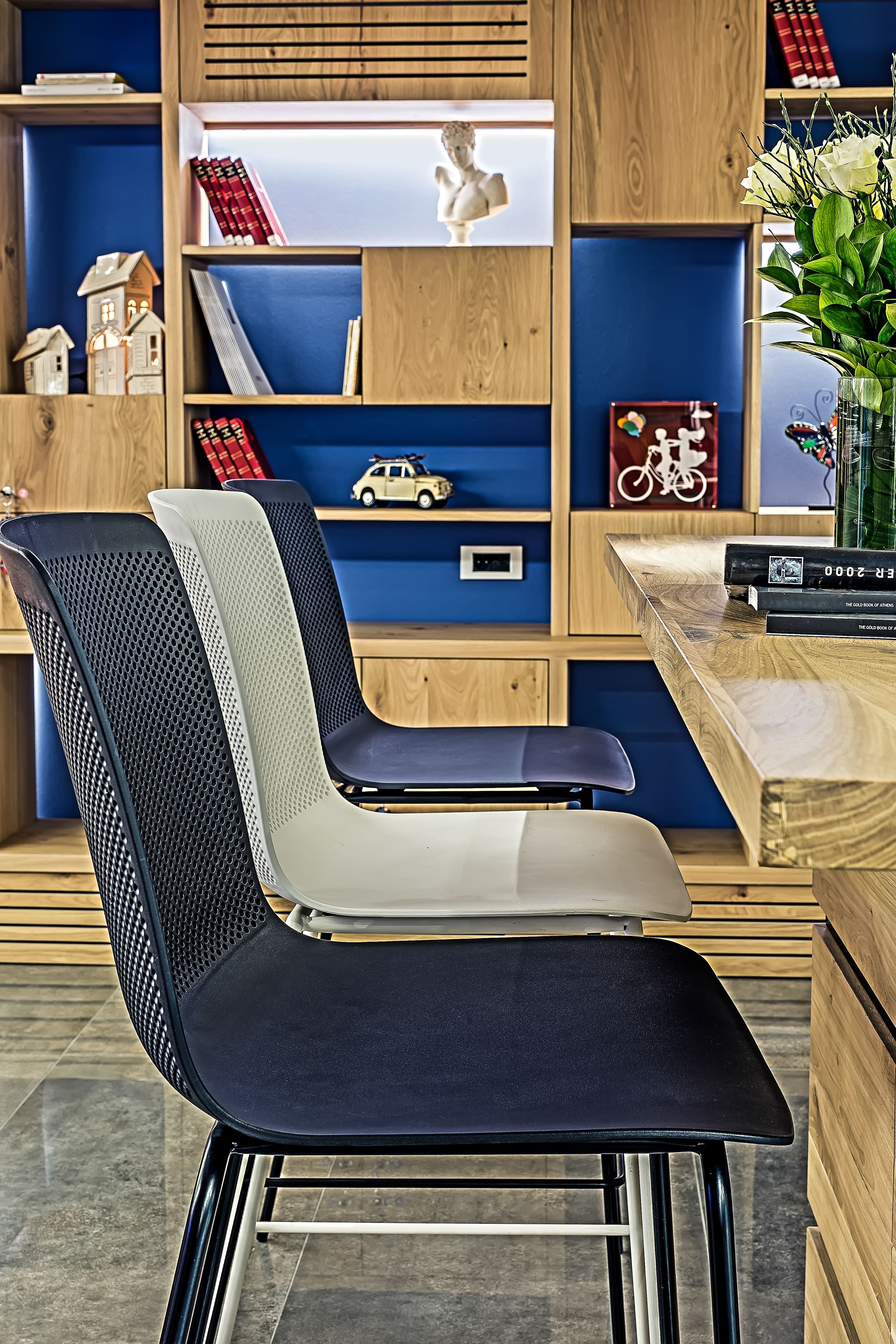 Una habitación moderna y bien organizada con un escritorio de madera, una silla con respaldo de malla y estantes con libros, un modelo de bicicleta y objetos decorativos.