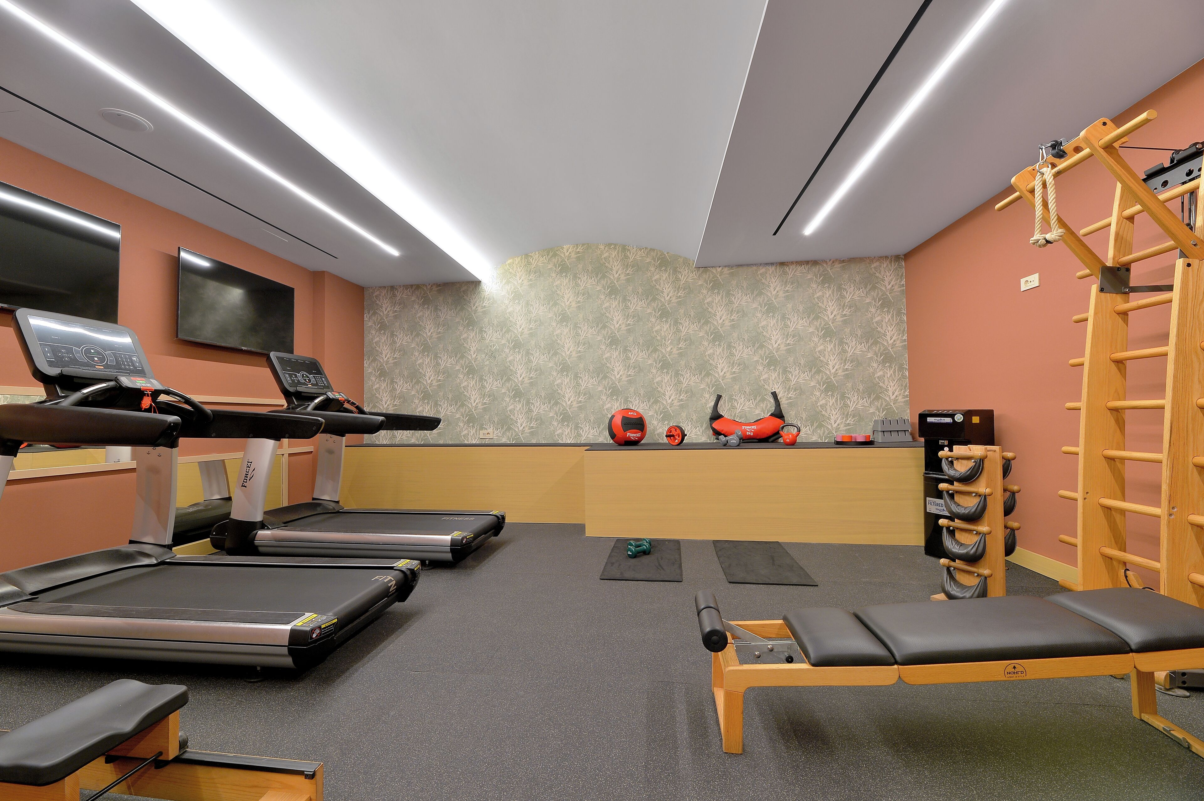 Une salle de sport équipée de tapis de course, d’un banc et d’une barre de traction.
